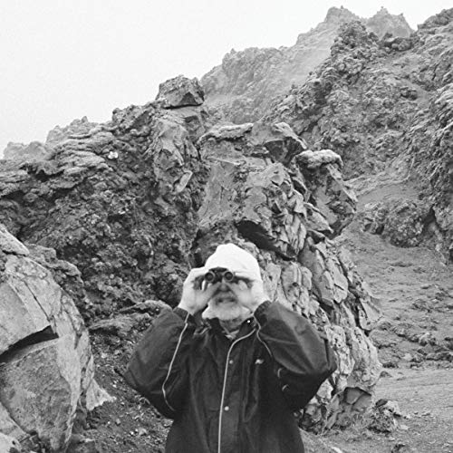 The alt text for the image is: "Black and white photo of a person standing in front of rocky terrain."