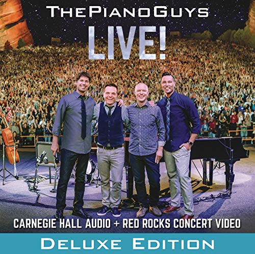 Four men standing on stage in front of a large crowd at Red Rocks.