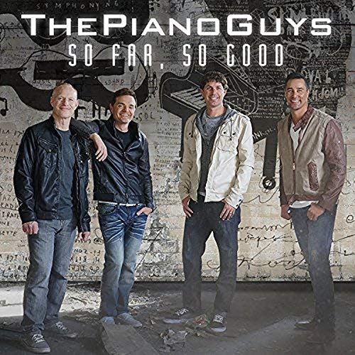 Four men stand in front of a wall with musical sketches and album text.