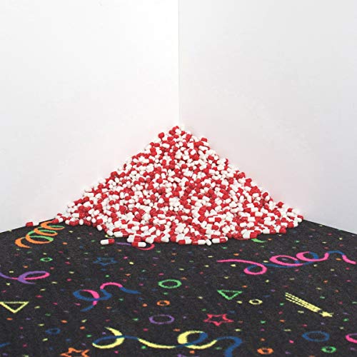 The image depicts a pile of red and white capsules on a black surface. * The key elements in the image are: * A large pile of red and white capsules * A black surface with multicolored confetti-like designs * A white wall in the background * The most concise description of the image is: "Red and white capsules piled on a black surface."