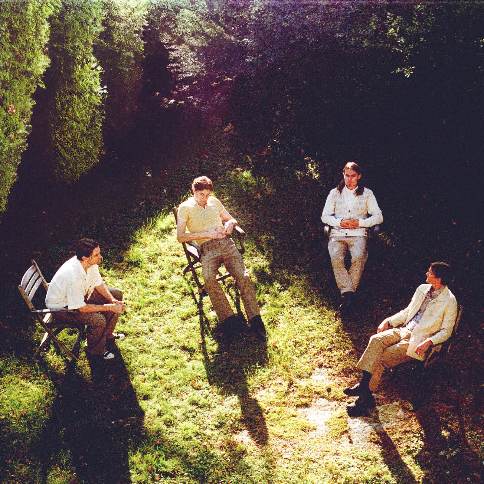 Four men sit in chairs arranged in a circle on a grassy lawn.