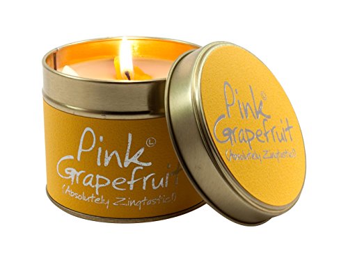 A lit Pink Grapefruit scented candle in a yellow tin with its lid beside it.
