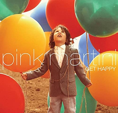 A young boy in a suit stands surrounded by many large, colorful balloons.