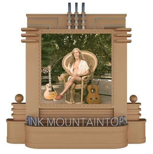 A man sits in a wicker chair between two guitars within an ornate frame.