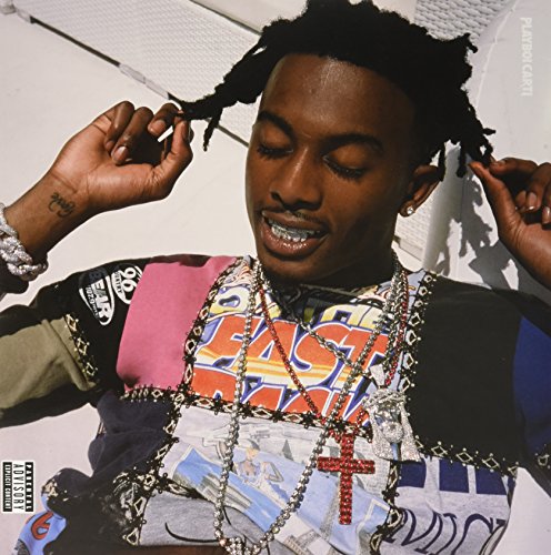 Playboi Carti wearing multiple necklaces and a patterned shirt, holding his hair with hands.