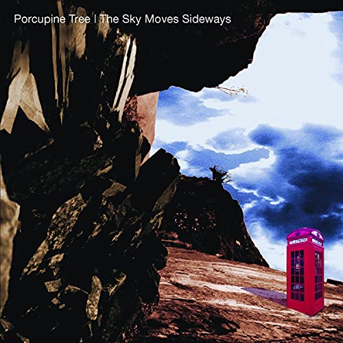 A red telephone box stands on a rocky landscape under a blue cloudy sky.