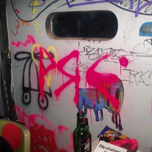 Graffiti on a wall with a small window, a beer bottle, and a snack bag.