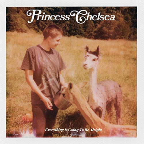 Princess Chelsea standing in a field feeding two alpacas from a metal bowl.