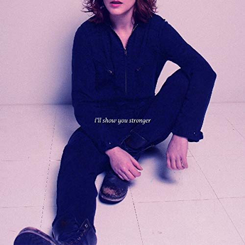A woman in dark blue jumpsuit sits on a white tiled floor, album cover displayed.
