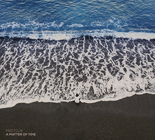 A person sits on a dark sand beach facing the ocean waves.