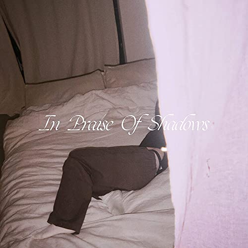 CD cover: a person sitting on a rumpled bed, pale pink tones.