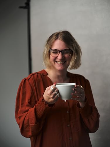 Smiling woman with glasses holding a white mug.