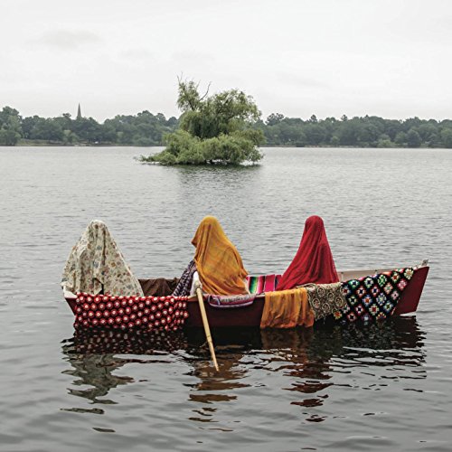"Three people in a boat on a lake, covered in colorful fabrics and quilts."