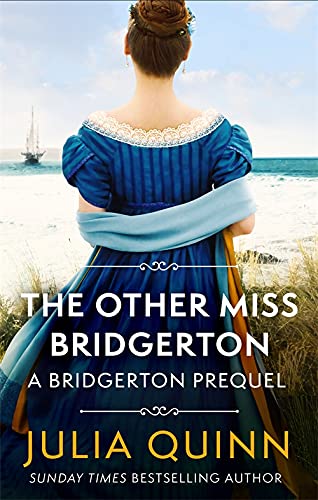 A woman in a blue Regency dress stands on a beach looking at a ship.