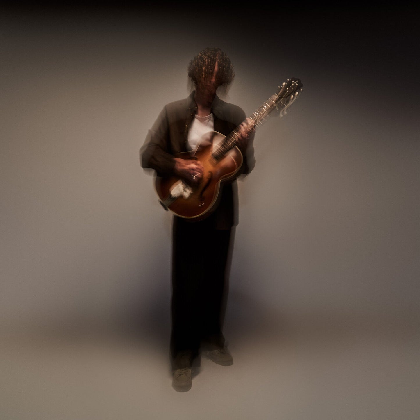 Musician with curly hair playing an acoustic guitar, blurred effect.
