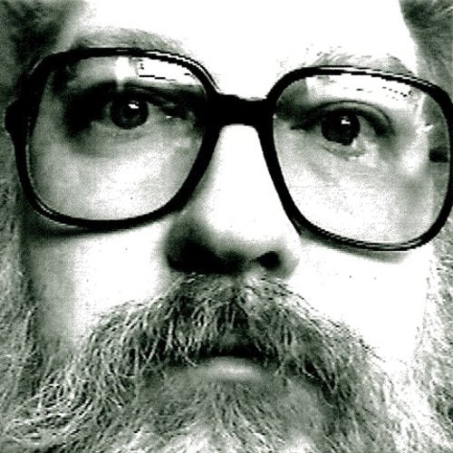 Black and white close-up of a bearded man wearing large dark-rimmed glasses.