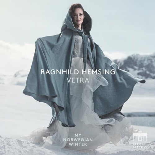 Woman in a blue cloak against a snowy, mountainous backdrop.