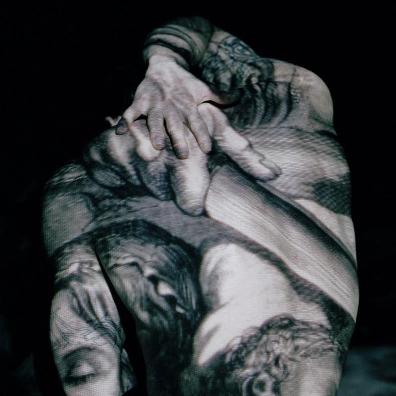 Black and white photo of a tattooed person’s back and hands.