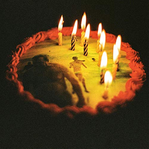 Overhead view of a birthday cake with lit candles and toy figures.