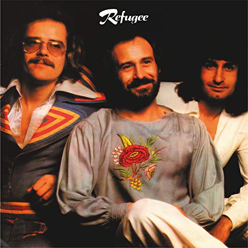 "Album cover featuring three men with dark hair, posing together against a dark background."
