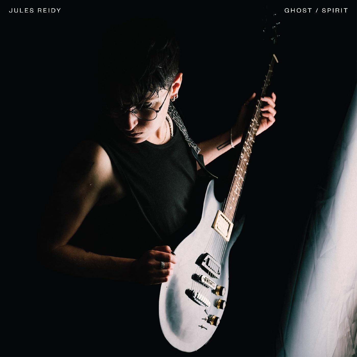 Musician with guitar, dark background, album cover for "Ghost/Spirit" by Jules Reidy.