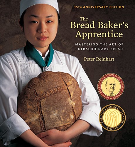 A baker in a white uniform holds a round loaf of crusty bread.