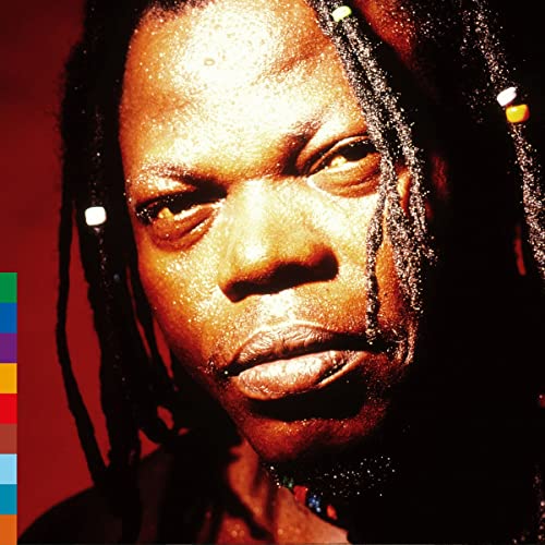 Close-up portrait of Remmy Ongala with dreadlocks against a red background.