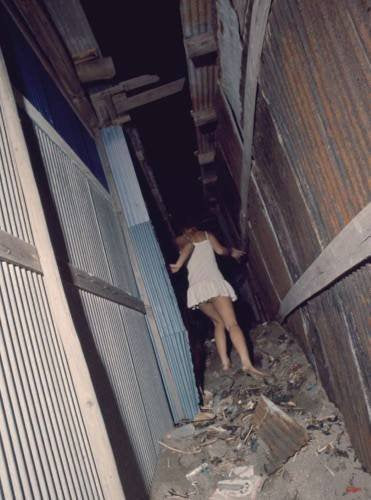Narrow alleyway with a person in a white dress walking away.