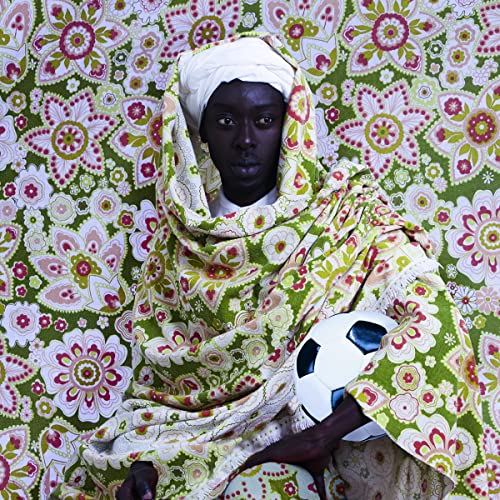 Man in headwrap holding a soccer ball, floral patterned background.