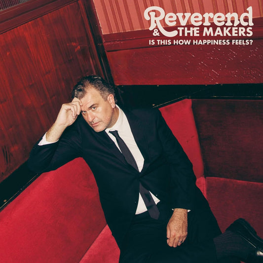 A man in a suit sits on a red booth with album text above.