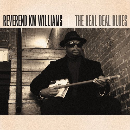 "Album cover featuring a man in a hat holding a guitar against a brick wall."