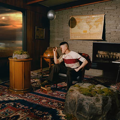 Rich Brian sits in a room with a globe and world map.