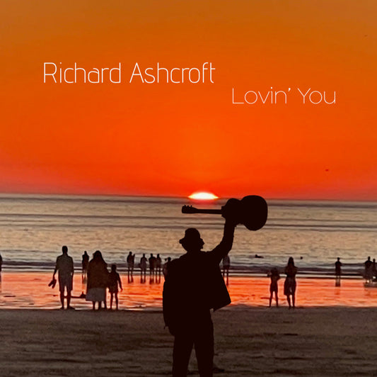 Silhouette of a man holding a guitar aloft on a beach at sunset.
