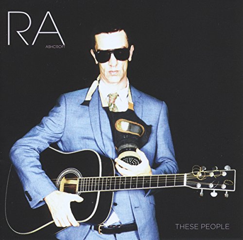 Man in blue suit and sunglasses holds guitar, wearing gas mask, against black background.