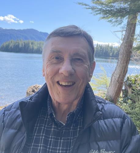 Smiling man outdoors with lake and mountains in the background.