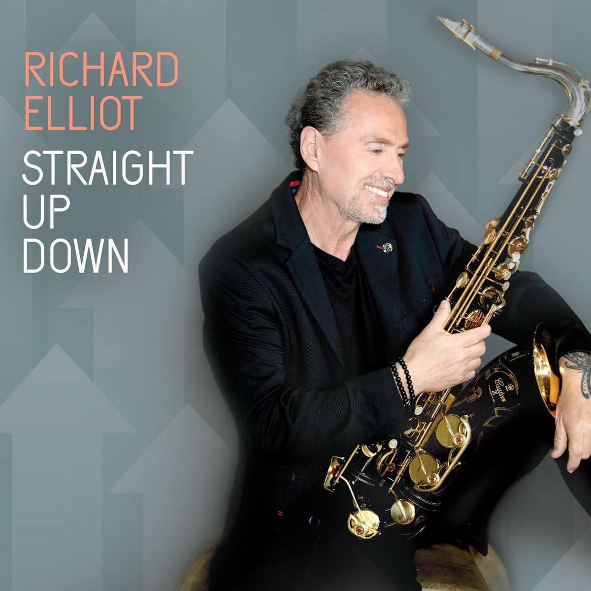 Richard Elliot smiling while holding a saxophone against a grey geometric background.