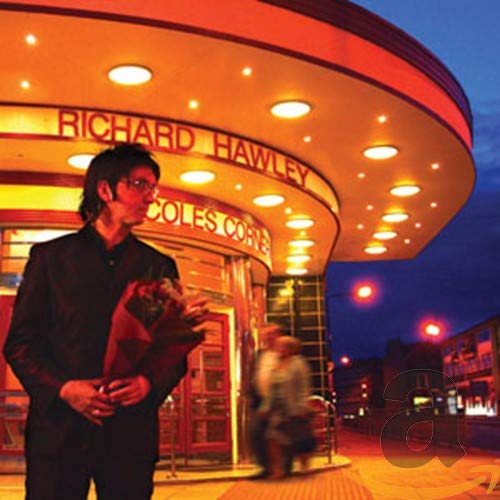 Richard Hawley stands before a lit art deco building facade.