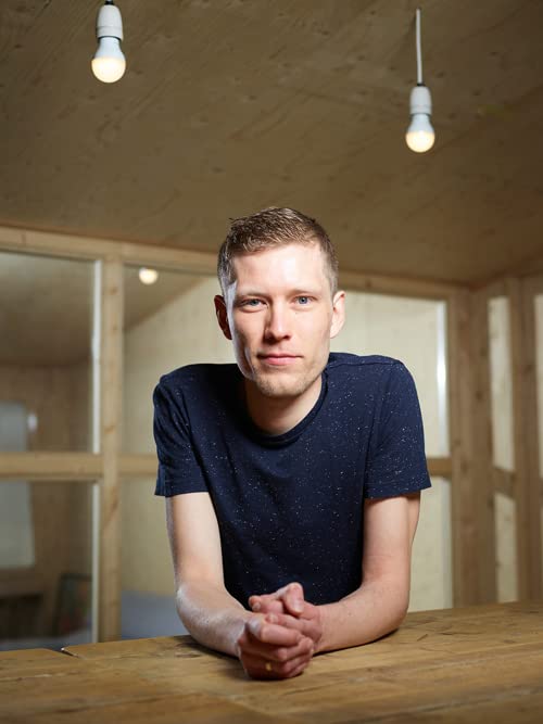 Young man with short blond hair in a simple interior setting.