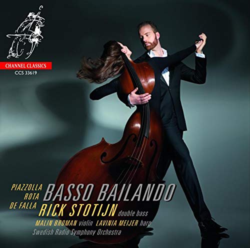 Man in black suit dancing with double bass on a dark background.