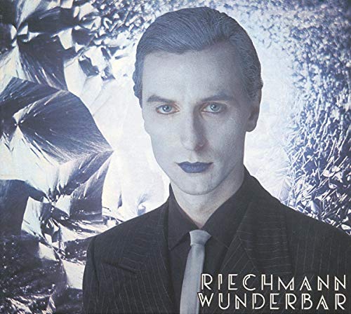 A pale man in a suit against a blue, crystalline background with album text.