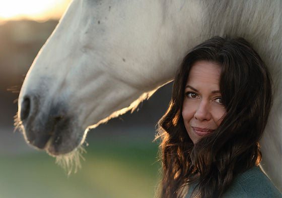 Woman with long brown hair leans against a white horse.