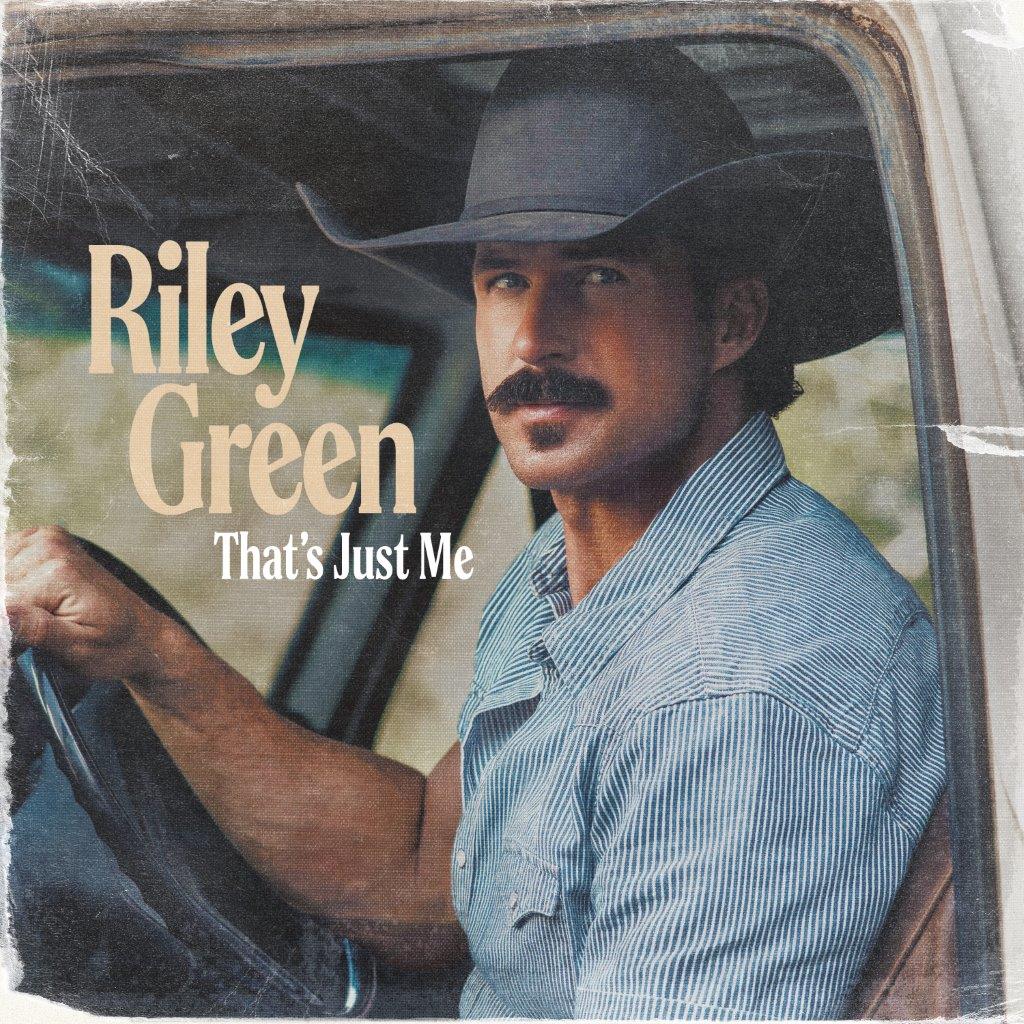 Riley Green wearing a cowboy hat and striped shirt, sitting in a truck.