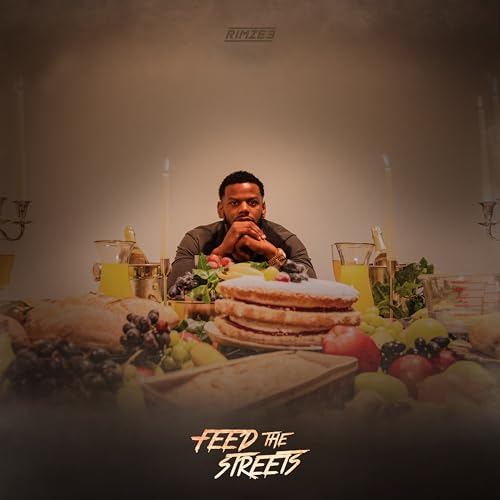 Rimzee sits at a table filled with food, fruit, and candles in a dark room.