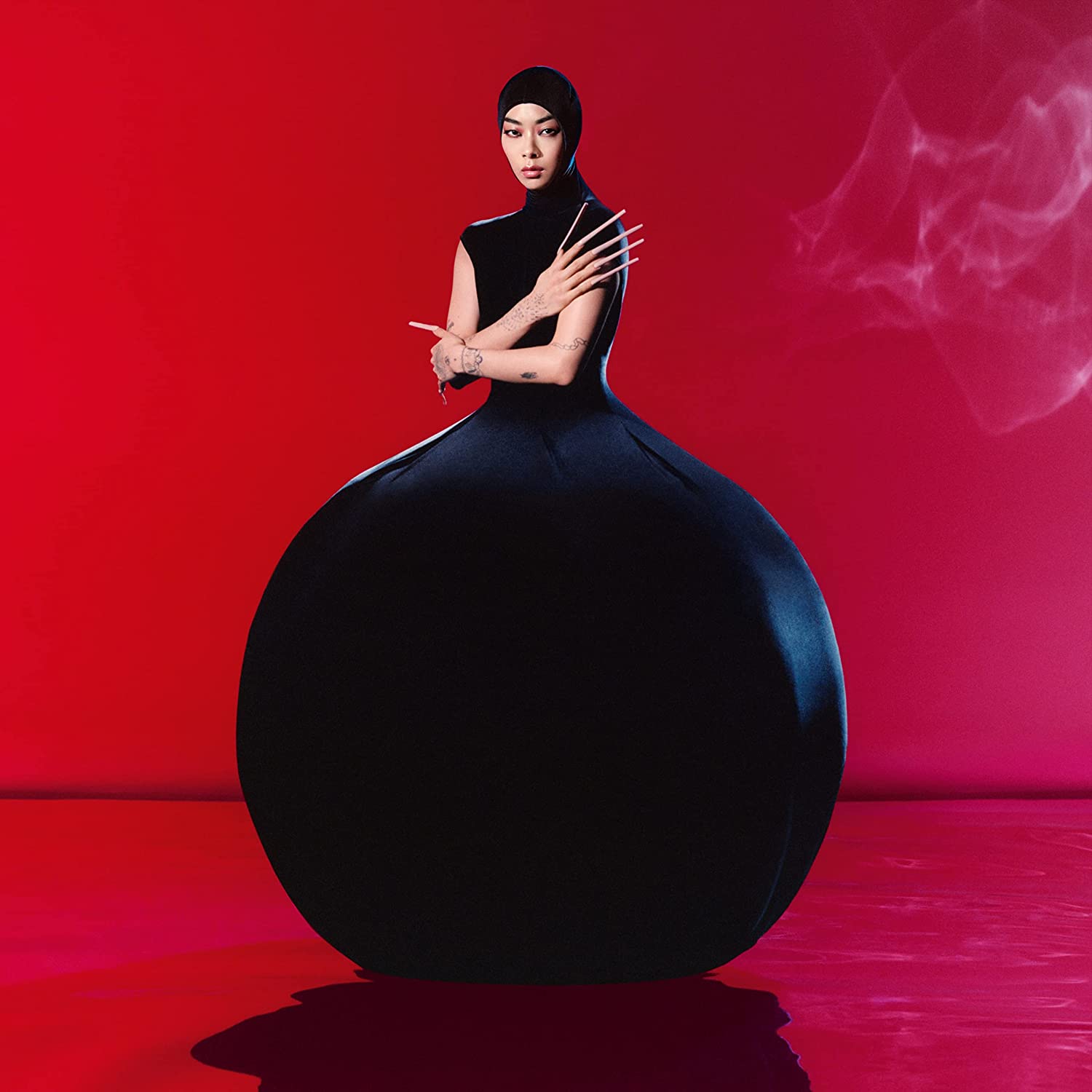 Rina Sawayama in a black, voluminous gown against a red background.