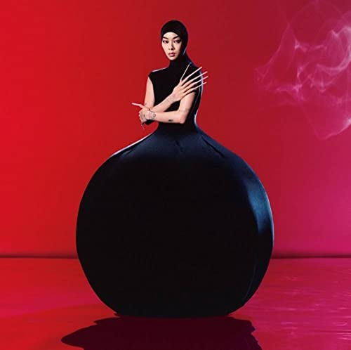 Rina Sawayama wearing a black, spherical gown against a bright red background.