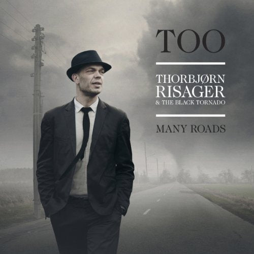 Album cover: man in a hat standing by a rural road.