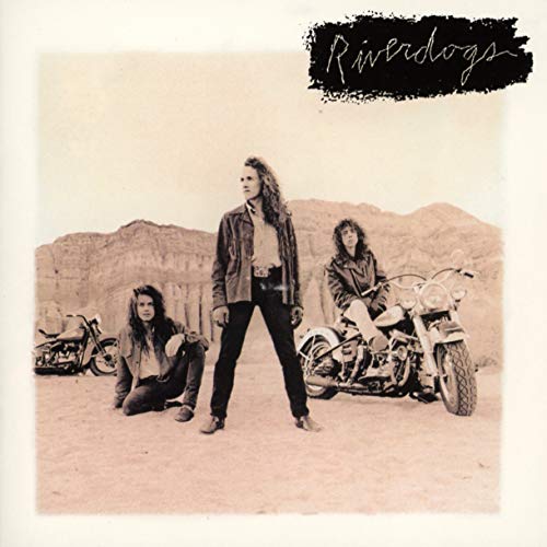 Three band members pose with motorcycles in a desert landscape under the band name Riverdogs.