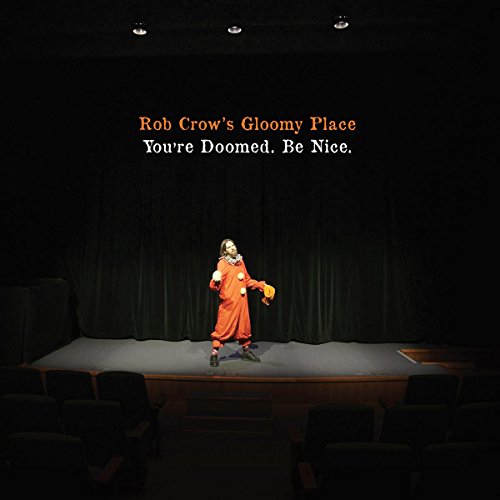 A person in a clown costume stands on a dark stage before empty seats.