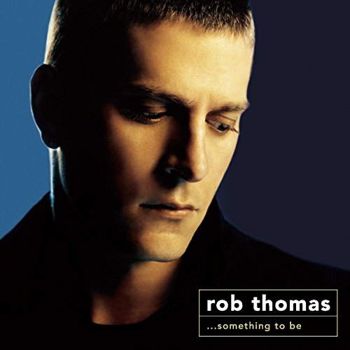 Close-up portrait of Rob Thomas looking down against a blue and black background.