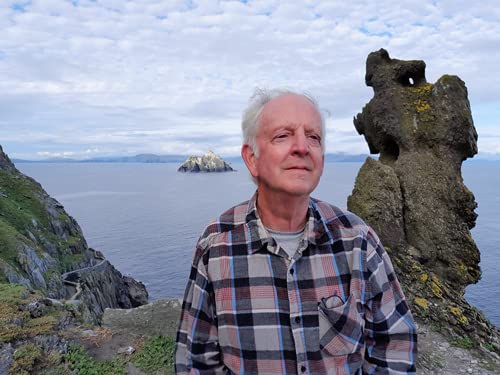 Man in plaid shirt stands on Skellig Michael overlooking the sea.